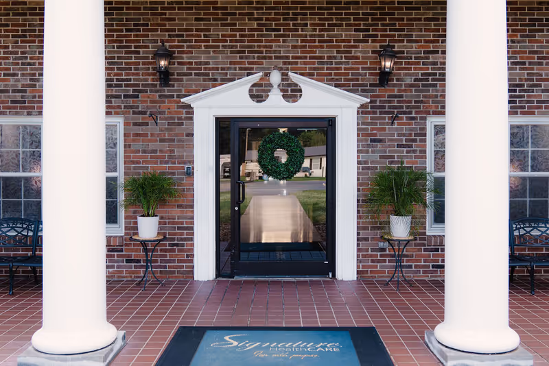 Front entrance of Signature HealthCARE of Glasgow with brick facade, columns, and a wreath.