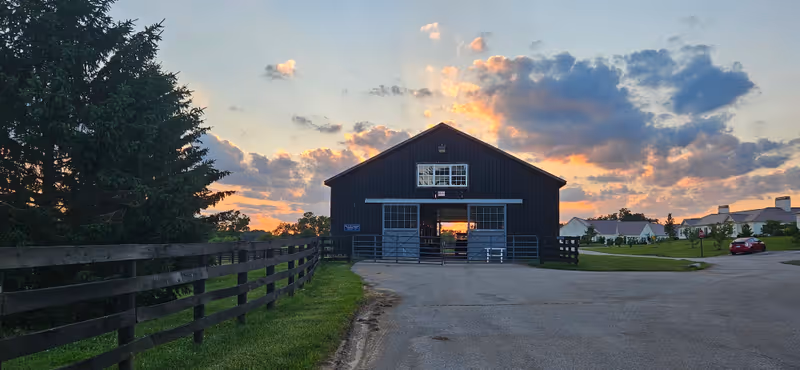 Sunset-lit exterior of a barn-style senior living facility with a fence and road.