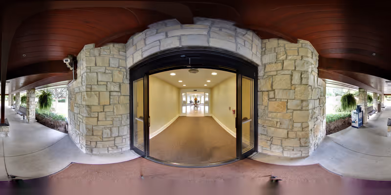 Covered stone entrance with glass double doors leading into a carpeted interior hallway.