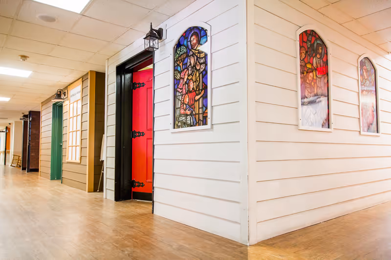 A bright hallway in a senior facility with colorful doors and stained glass windows.
