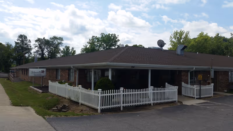Front view of Salyersville Nursing and Rehab, brick building with white picket fence and covered entrance.