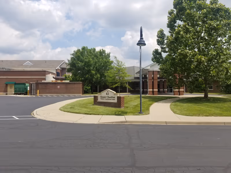 Front view of Kosair Charities Pediatric Convalescent Center with sign, trees, and driveway.