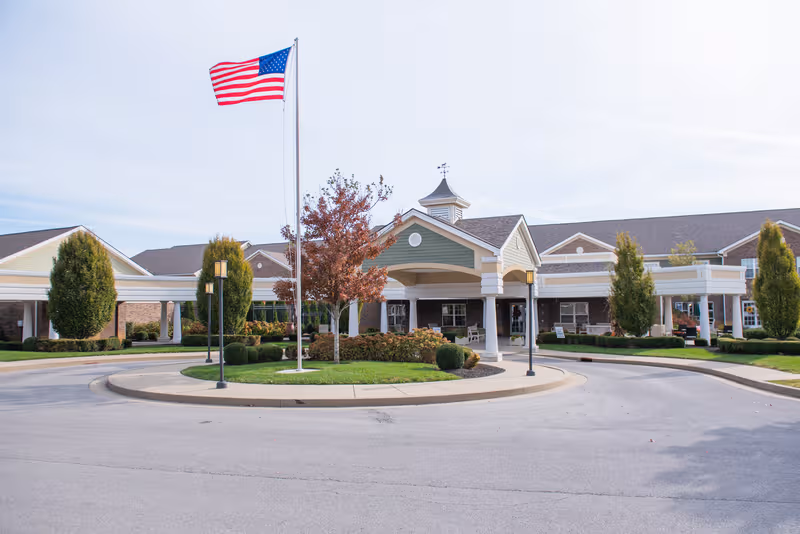Exterior view of Bridgepointe at Ashgrove Woods with flag, circular driveway, and main entrance.