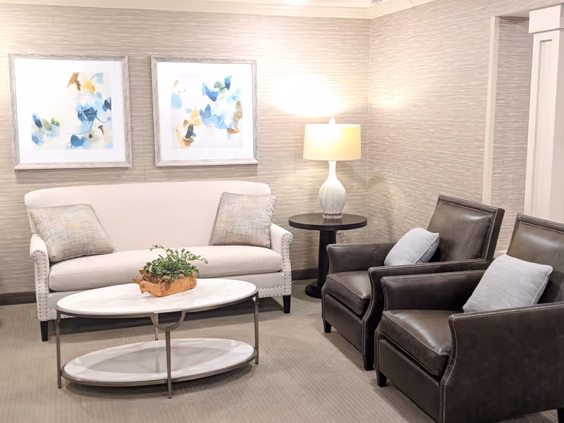 Cozy lounge area with a white sofa, two dark leather chairs, coffee table, and wall art.