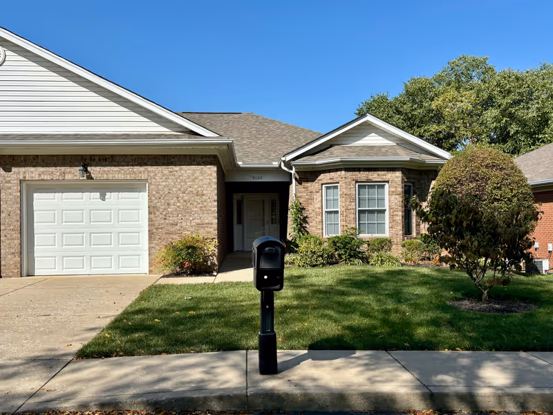 Front exterior of a single-story brick home with an attached garage, driveway, mailbox, and landscaped lawn.