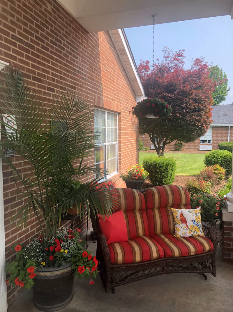 Outdoor porch with striped wicker sofa, cushions, and potted flowers.