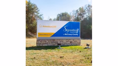 An outdoor sign for Signature HealthCARE of McCreary County stands on a grassy lot.