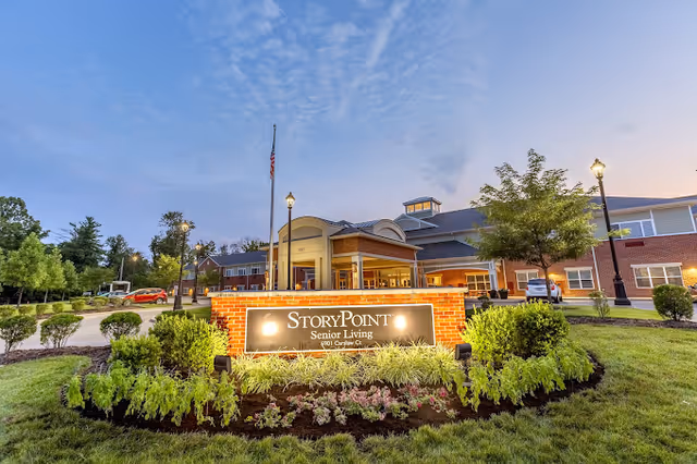 Front exterior of the StoryPoint Senior Living building with an illuminated sign and landscaped entrance at dusk.