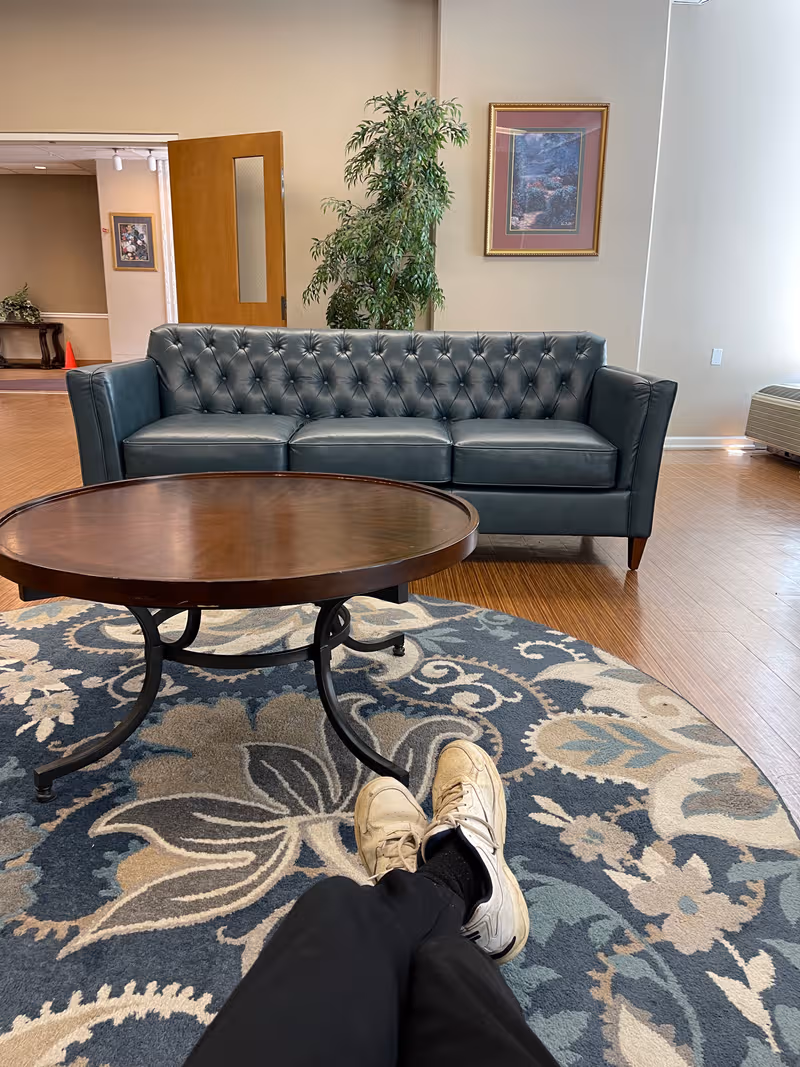 Lounge area in a senior facility with sofa, coffee table, rug, and plant.