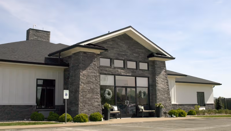 Exterior view of Peridot Senior Living with stone facade, glass entry, and planters.
