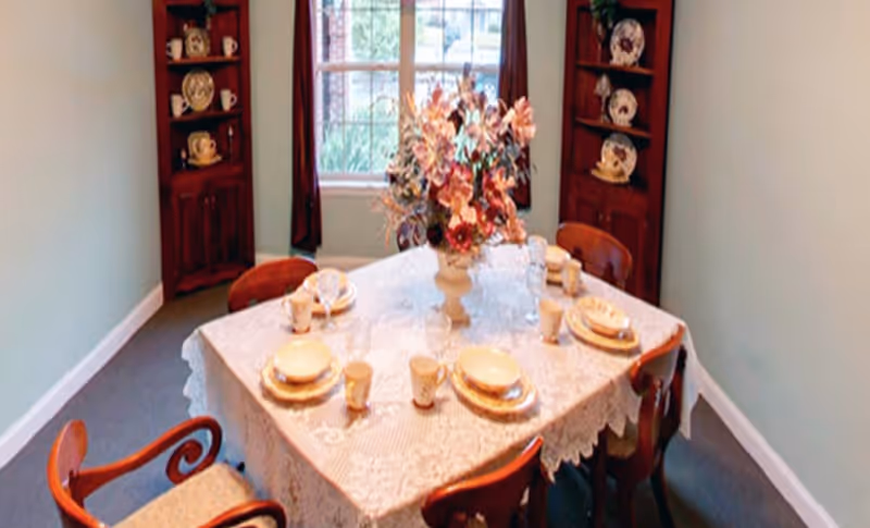A dining room with a lace tablecloth, floral centerpiece, and place settings.