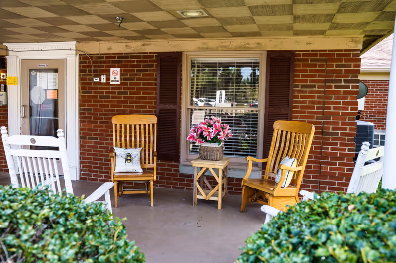 Brick exterior porch with two wooden rocking chairs and a small table with flowers.