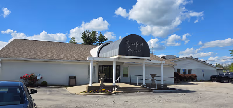 Front view of Bradford Square senior living facility entrance with awning and parking lot.