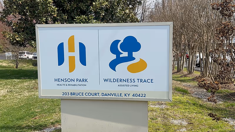 Outdoor sign shows Henson Park Health & Rehabilitation and Wilderness Trace Assisted Living logos.