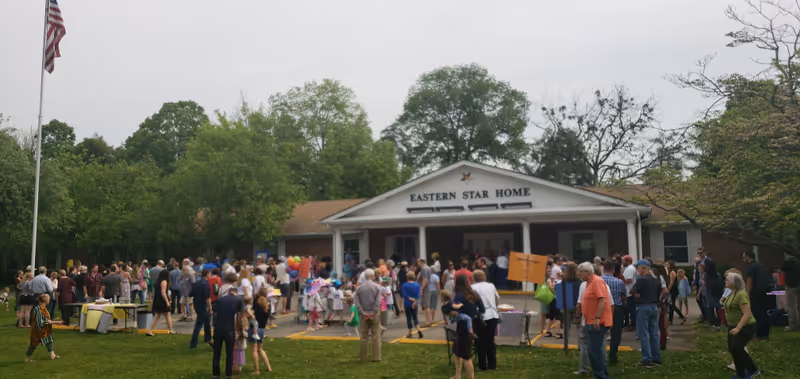 A large crowd gathers outside the Eastern Star Home building for an outdoor event.