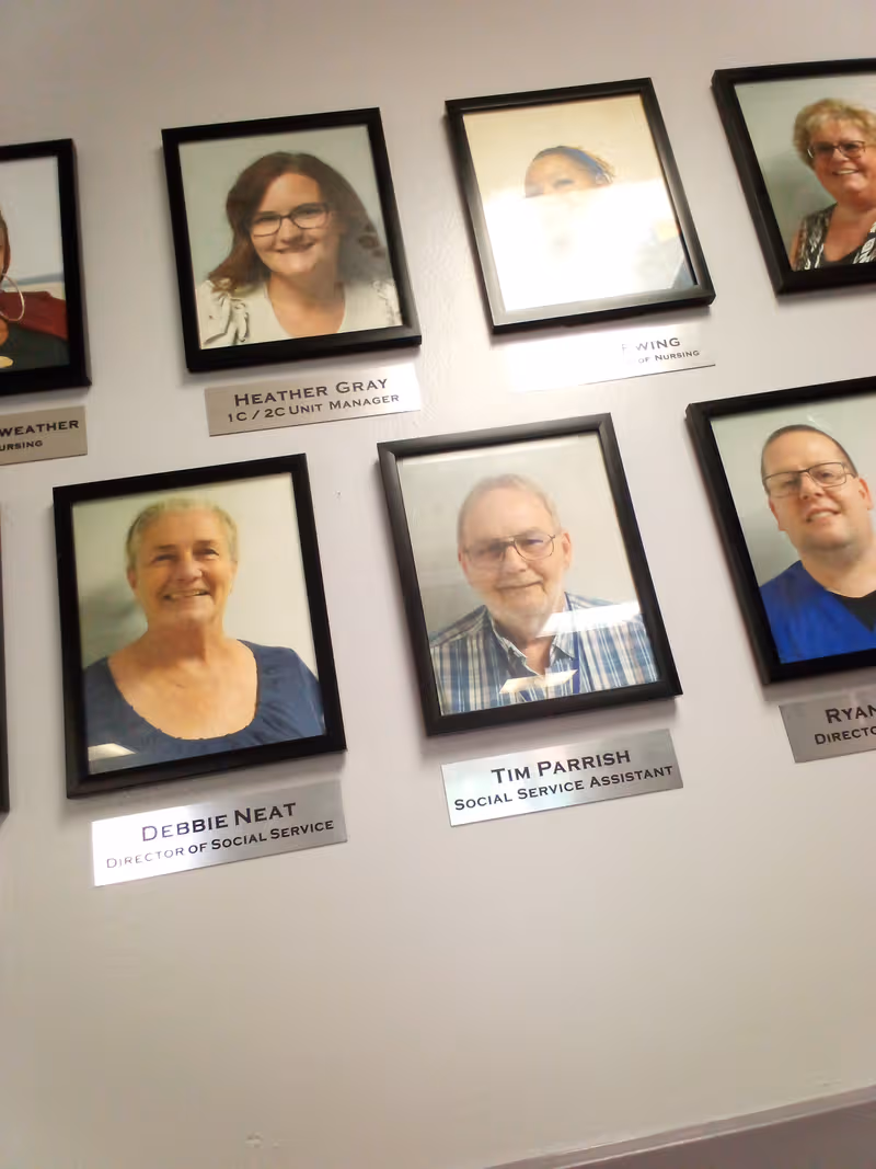 Wall with framed staff portraits and silver nameplates in an interior hallway