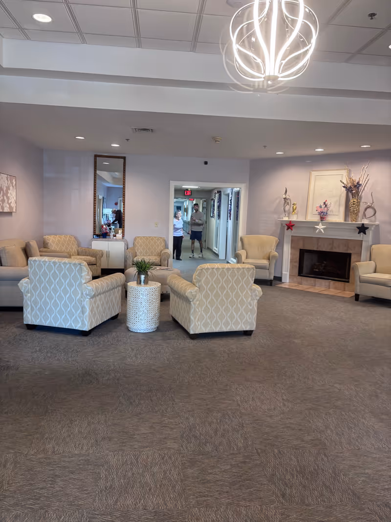 Spacious lounge area with patterned chairs, a fireplace, and decorative mantle in a senior living lobby.