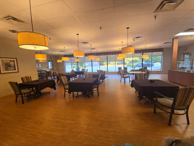 A spacious dining area with multiple tables, chairs, and warm pendant lights.