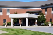 Front entrance of a two-story brick healthcare building with a covered porte-cochere, columns, and landscaping.