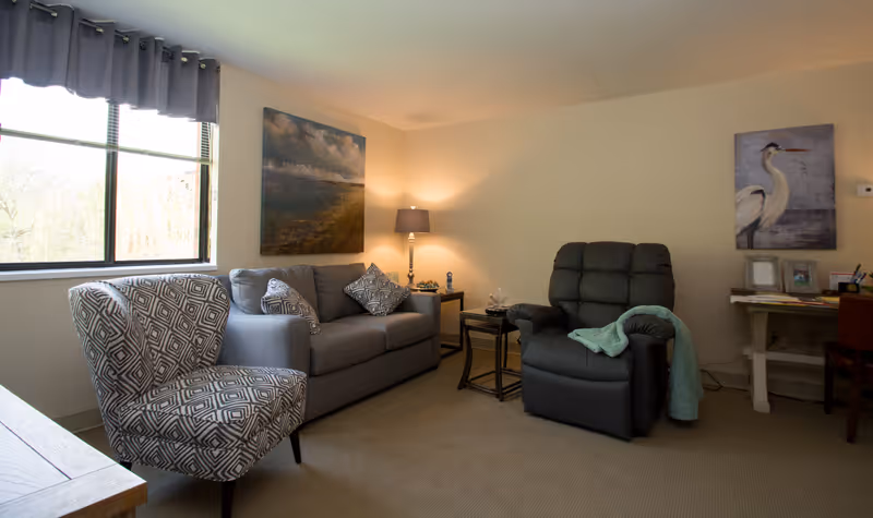 Living room with a patterned armchair, gray sofa, recliner, side tables, lamp and wall art.