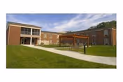 Two-story brick senior living building with a central courtyard, pergola, walkways and grassy lawn under a partly cloudy sky.