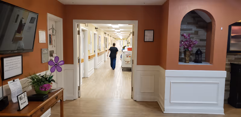 Interior hallway at Hermitage Care and Rehabilitation Center with a staff member walking.