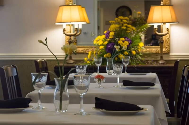 Dining room table set for service with glassware and floral centerpiece.