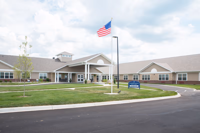 Front exterior of Sanders Ridge Health Campus showing the entrance, an American flag on a flagpole, and a circular driveway.