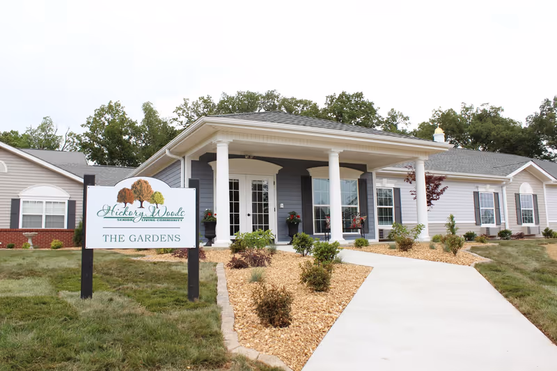 Front view of Hickory Woods Senior Living entrance with sign and landscaped walkway.
