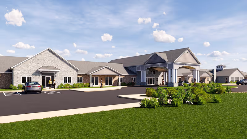 Exterior view of Cedarhurst Senior Living of Nicholasville building with a large covered entrance, parking spaces, green lawn, and a few people walking near the entrance under a partly cloudy sky.