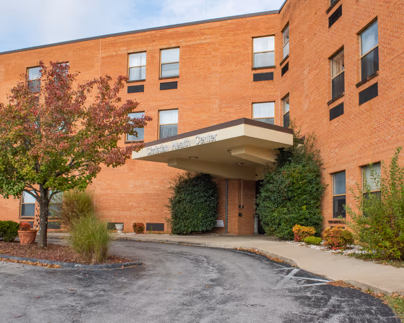 Front entrance of a brick senior care building with a covered portico reading 'Christian Health Center', landscaped shrubs and a curved driveway.