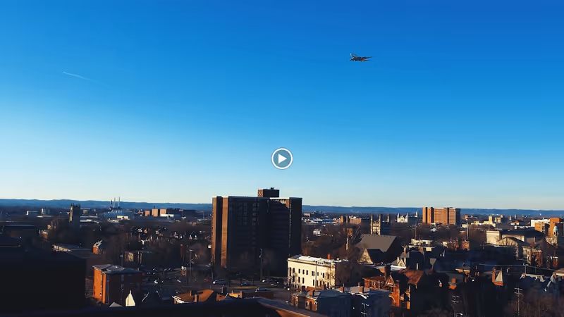 Cityscape view with multiple buildings under a clear blue sky and an airplane flying overhead.