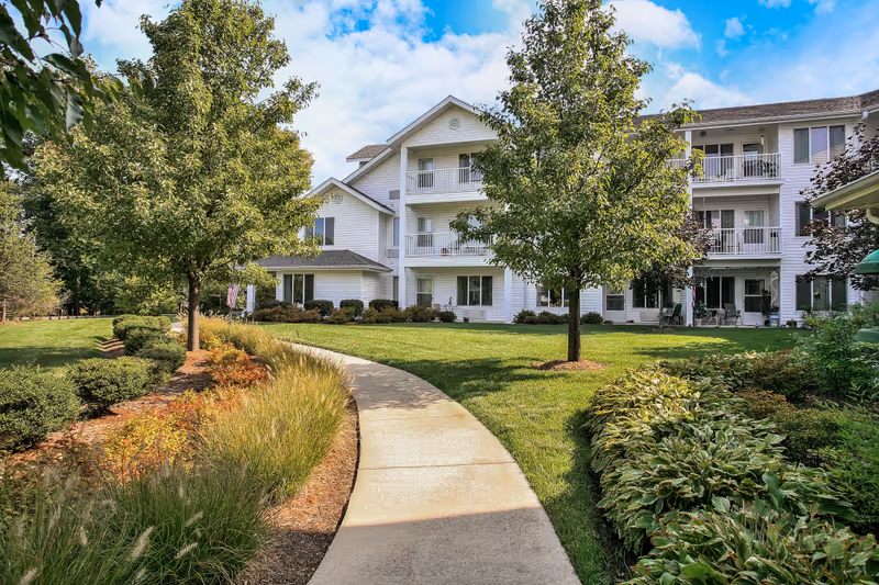 White multi-story senior living building with balconies, green lawn, and curved concrete path.