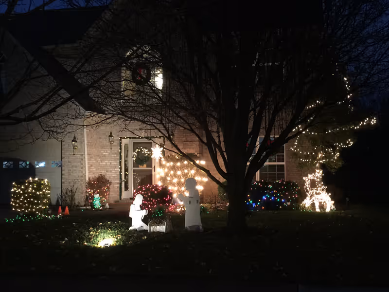 Night view of a brick senior living facility front yard with holiday lights and decorations.