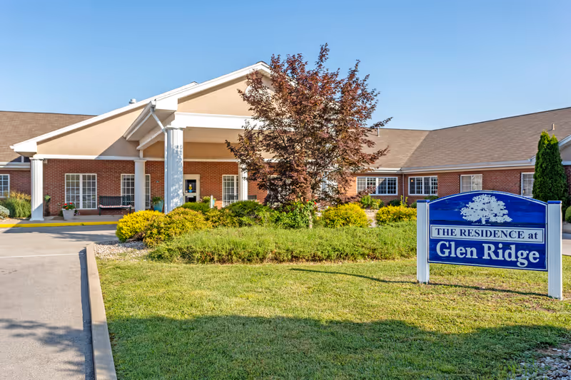 Front entrance of the Glen Ridge health campus with a covered portico, landscaped lawn, and a blue sign reading "The Residence at Glen Ridge".