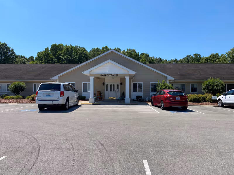 Front view of a single-story senior living facility with a main entrance and parking.