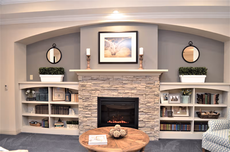 Cozy living room with a stone fireplace, built-in shelves, and framed artwork.