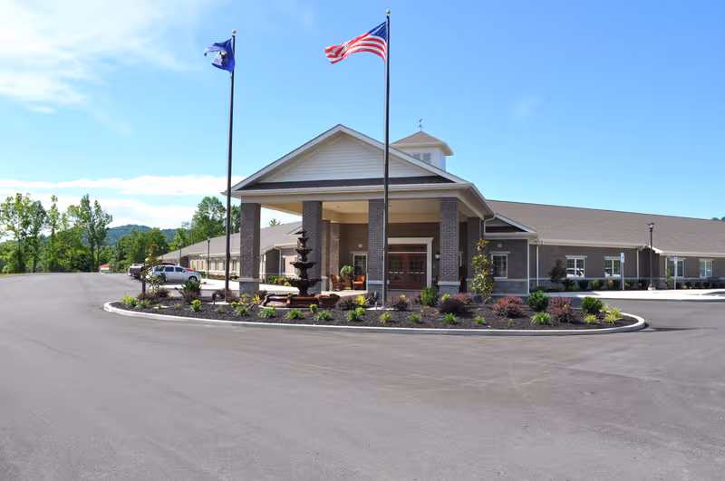 Exterior view of Barbourville Health and Rehabilitation Center with flags, entryway, and landscaped island.