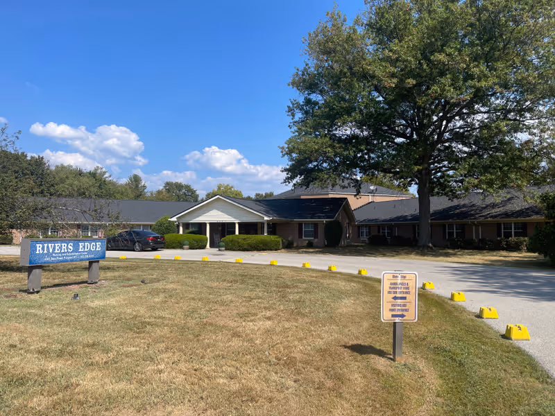 Exterior view of Rivers Edge Nursing & Rehabilitation Center with a sign and surrounding landscaping.