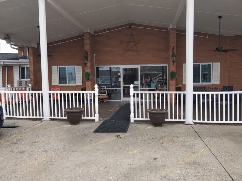 Brick senior living facility entrance with a covered porch and white railing.