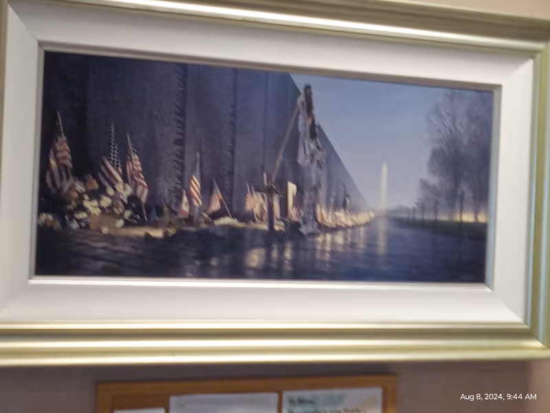 Framed artwork on a wall depicts a memorial scene with flags and water reflections.