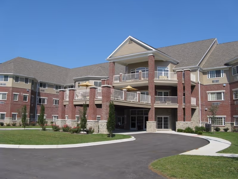 Front exterior of a multi-story brick senior living building with balconies and a covered main entrance.