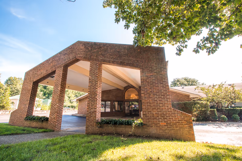 Brick building with a covered front entrance and surrounding landscaping.