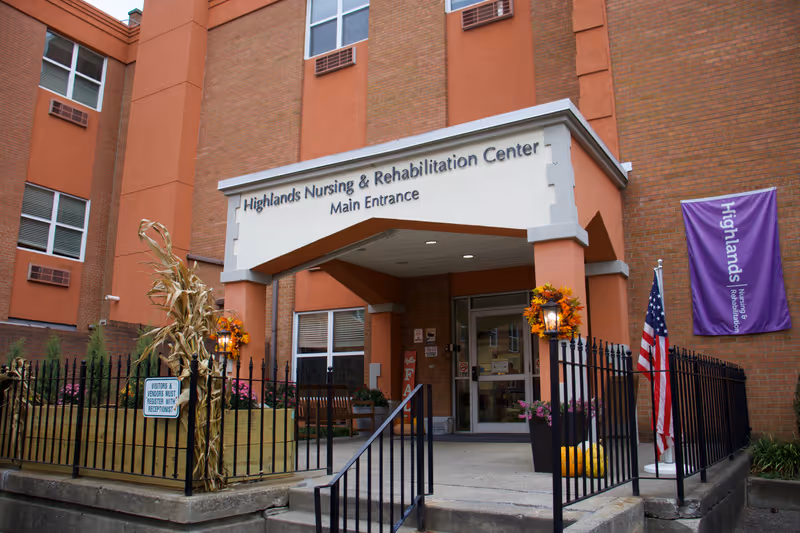Front exterior view of Highlands Nursing & Rehabilitation Center main entrance with walkway and flag.