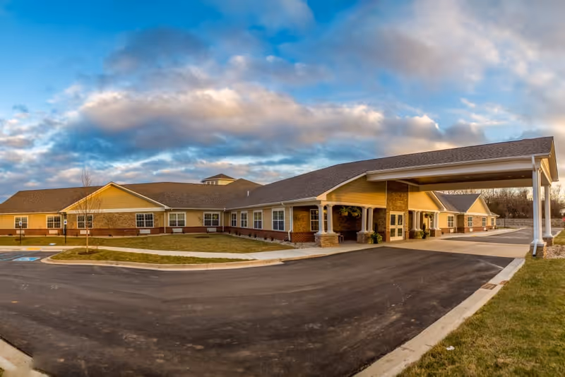 Exterior view of The Willows at Fritz Farm building with a covered entrance, parking area, and a partly cloudy sky.