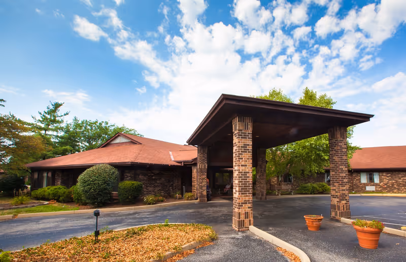 Front exterior of a brick senior care building with a covered porte-cochère and driveway.