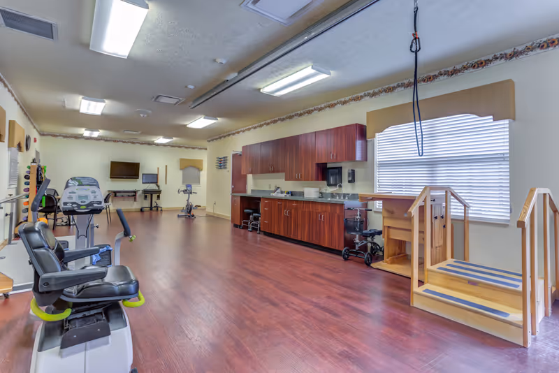 Spacious senior living facility exercise room with cardio machines and a kitchenette.