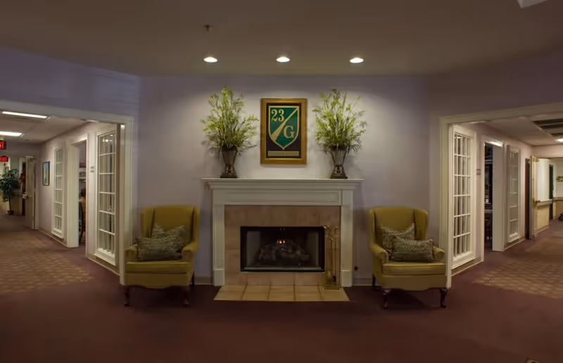 Cozy interior lobby with a fireplace, two yellow armchairs, and side hallways.