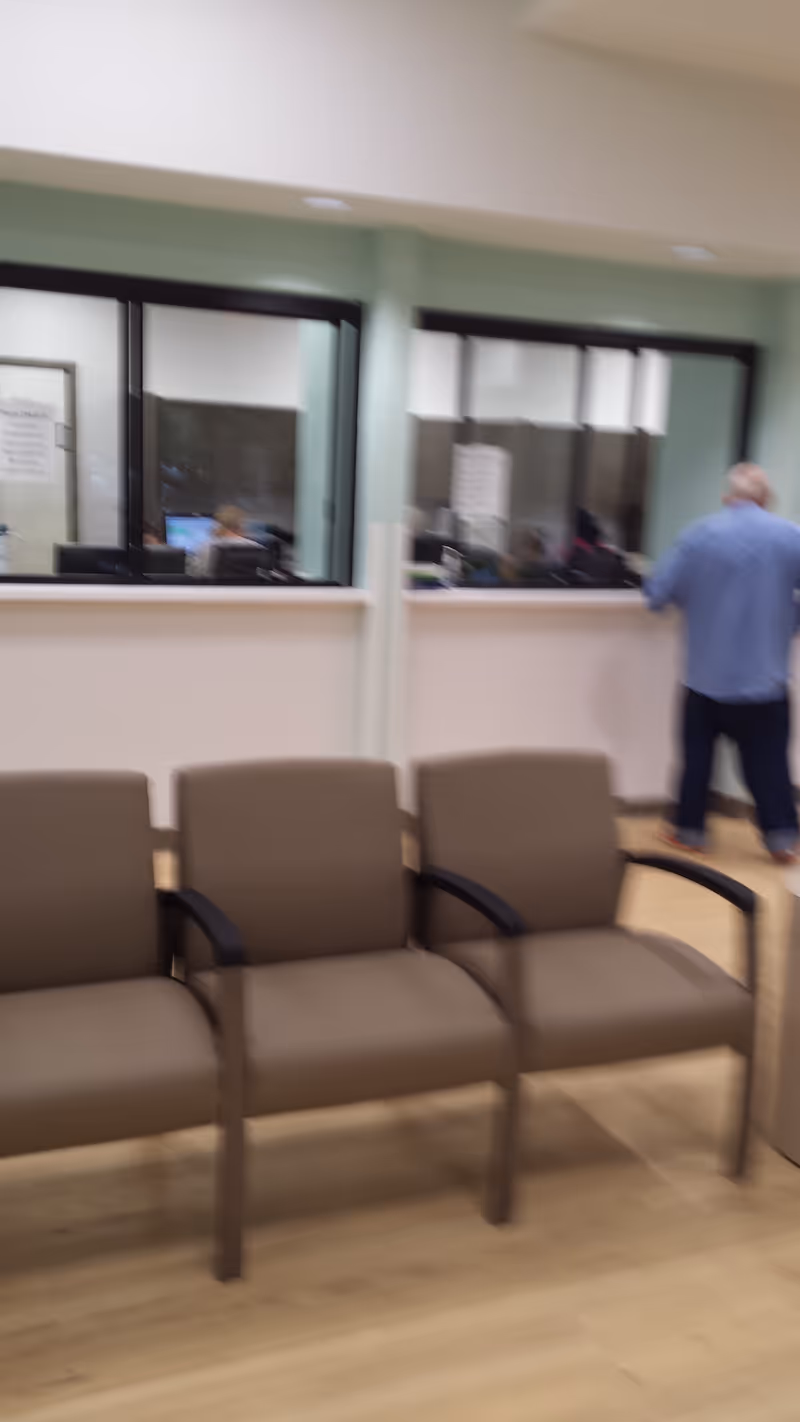Blurred indoor waiting area with beige chairs and a reception window behind.