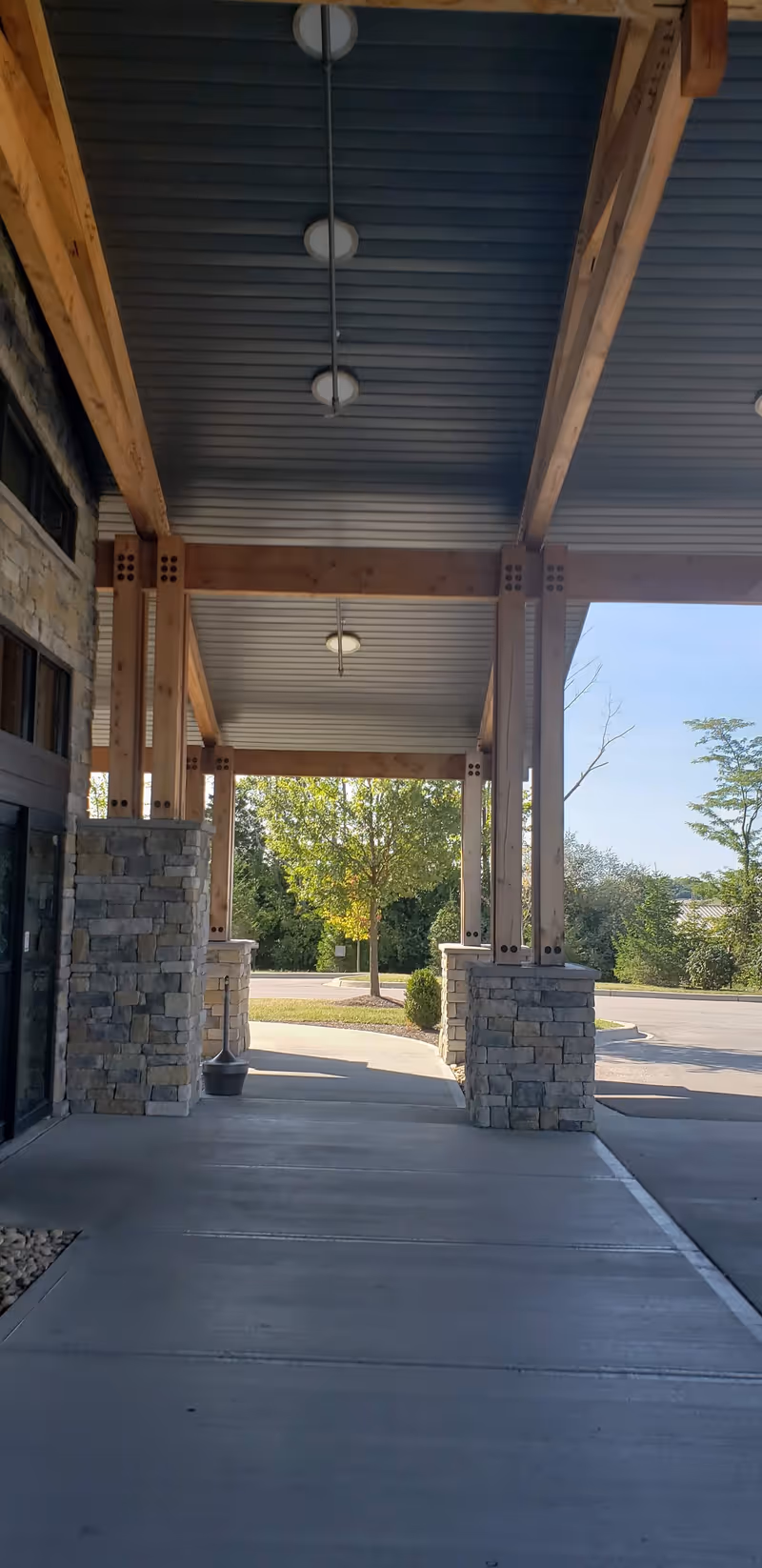 Exterior walkway at Boonespring Skilled Nursing Facility with wooden beams and stone columns.